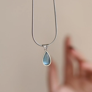 Macro shot of blue teardrop gemstone pendant on silver snake chain necklace