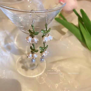 Detail showing lily of the valley earrings with pearls hung on a glass in soft light