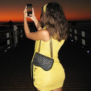 Close-up of a yellow knitted dress and a black quilted chain bag in an outdoor setting