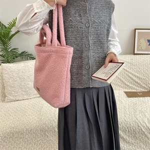 Detailed shot of pink plush tote bag with brown leather tag carried by a model