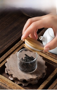 Close-up of glass tea canister with wooden lid and base beside a ceramic teapot