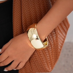 Close-up of a wide chunky gold polished cuff bracelet worn on the wrist against woven texture