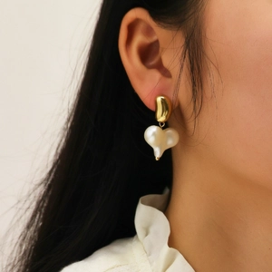 Detailed close-up of a gold heart pearl earring on a model with elegant styling