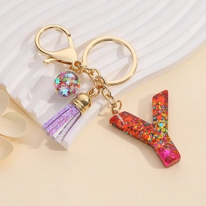 Detail of colorful glitter letter Y keychain with purple tassel and gold ring on white pedestal