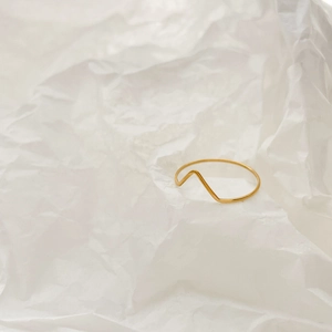Detailed view of minimalist gold thin wavy ring on an artistic white paper texture background
