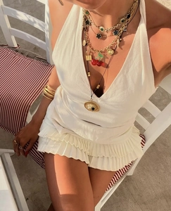 Detalle de vestido blanco halter con volantes y collares de capas con dijes de trébol