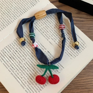 Detailed view of handmade knitted cherry pendant and blue ribbon necklace on a book