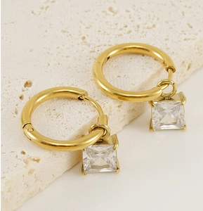 Detail of gold hoop earrings with square clear zircon pendants on white stone