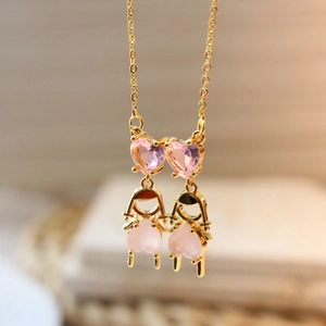 Gros plan d'un collier doré avec pierres de cœur roses et détails de breloques filles