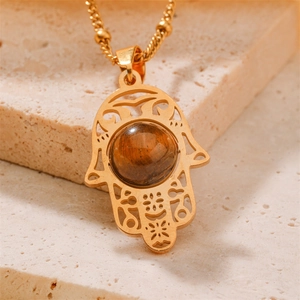 Golden Hamsa hand necklace with tiger eye stone pendant on natural stone base