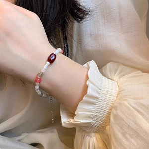 Detail view of a colorful beaded bracelet with a deep red oval gem on a woman's wrist