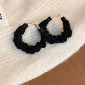 Close-up of black fuzzy textured hoop earrings with gold needles on knitted background
