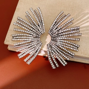 Detail of silver fan-shaped geometric earrings with sparkling white rhinestones on a book
