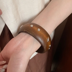 Détail d'un large bracelet en bois avec rivets argentés et étoile sur le poignet