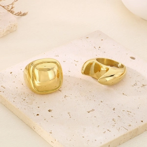 Macro view of gold plated chunky square signet and fluid asymmetric rings on stone