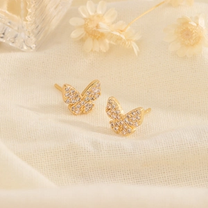 Exquisite gold butterfly stud earrings with zircon inlay on a warm textured background