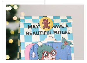 Close-up of light blue checkered Christmas gift bag with snowman illustration and sticker
