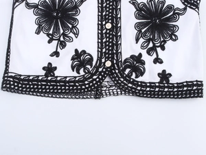 Detail of white ethnic vest with black floral embroidery and lace crochet hem design