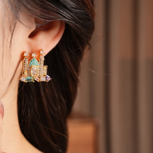 Detail of gold-plated castle earring with colorful gemstones worn by a model