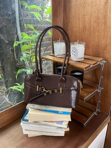 Detail of a dark brown glossy leather shoulder bag with long straps on a wooden stand