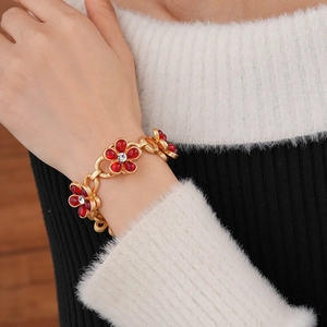 Close-up of gold chain bracelet with red glass flowers and crystal centers on a wrist