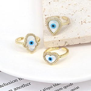 Detailed macro view of gold heart and hamsa rings with devil eye zircon and shell inlays