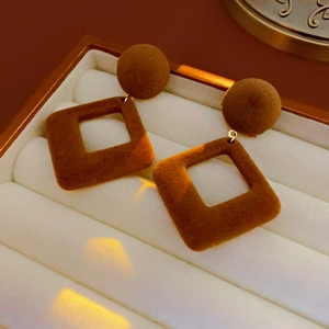 Détail de boucles d'oreilles géométriques en velours marron dans une boîte à bijoux