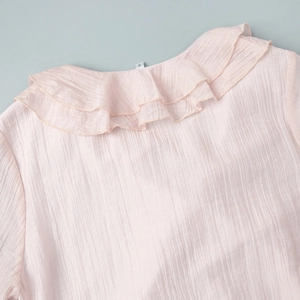 Close-up of ruffled V-neckline on a light pink dress with fine vertical pleated texture