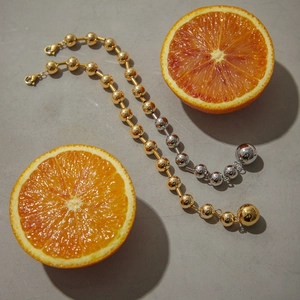 Bracelet et collier à billes en laiton doré et argenté présentés avec une orange fraîche