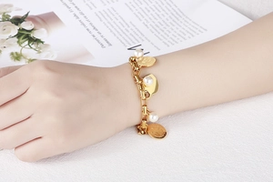 Gros plan d'un bracelet doré en acier inoxydable avec cœurs et perles blanches sur mannequin
