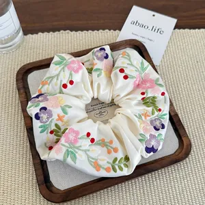 Elegant cream white satin scrunchie with colorful floral embroidery on a wooden tray
