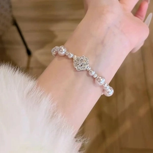 Détail d'un bracelet en perles avec breloque rose argentée porté sur une manche en peluche