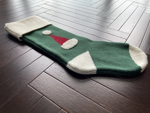 Detail of green knitted Christmas stocking with white cuff and red hat patch on wood floor