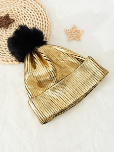 Metallic gold knit beanie with large black pompom on a cozy white plush background