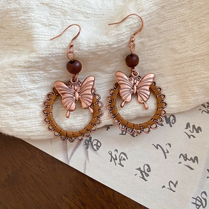 Macro detail of retro butterfly earrings with bronze metal and woven round hoops