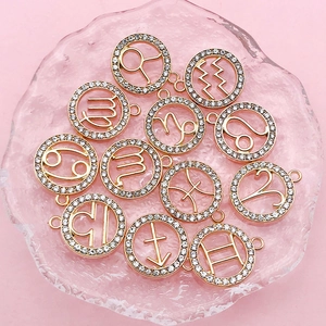 Macro shot of twelve golden zodiac pendants with sparkling crystals on a pink surface