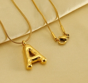 Detailed view of golden balloon-style letter A pendant on a sleek snake chain necklace
