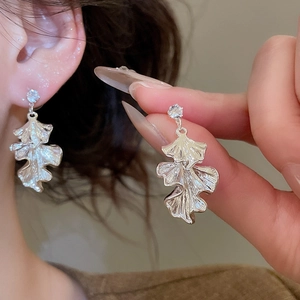 Close-up of silver ginkgo leaf earrings with liquid metal texture and clear gemstone