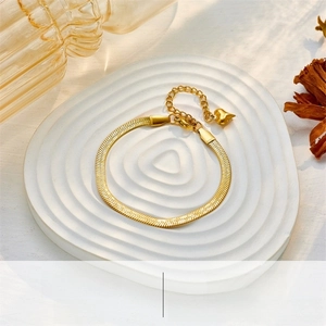 Detail of a gold snake bone chain bracelet with heart charm on a decorative tray