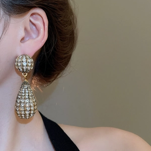 Close-up of gold hollow teardrop earrings with crystals worn by a model in a warm setting