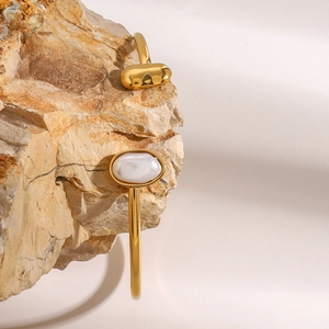 Detail of gold-plated stainless steel cuff bracelet with white pearl on natural rock