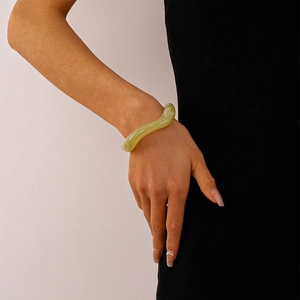 Irregular light green acrylic bangle with wave design worn over a black knit sleeve