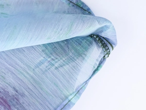 Detailansicht von Ölgemälde-Blumenmuster auf Chiffon-Stoff mit grüner Overlock-Naht-Verarbeitung