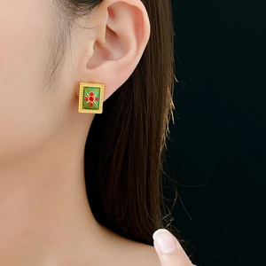 Close-up of vintage gold earrings with green base and red gemstones on model