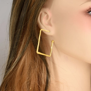 Close-up of model wearing large golden rectangular spiral earrings with metallic texture