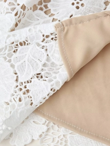 Détail de la dentelle florale blanche et de la doublure beige sur la robe longue