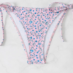 Close-up of pink floral bikini bottom with side ties on a white marble surface