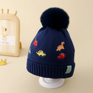 Détail de la texture en maille avec broderie dinosaure et grand pompon sur le bonnet