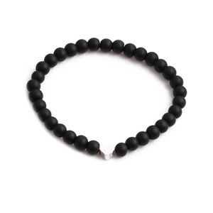 Bracelet en perles de pierre noire mate avec un pendentif cœur argenté sur fond blanc