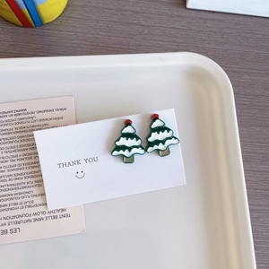 Détail de boucles d'oreilles sapin de Noël en émail coloré sur un plateau blanc